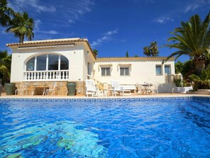 Relax by the villa's large pool surrounded by lush greenery and palm trees.