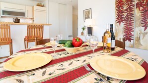 Een eethoek met een tafel gedekt voor twee personen, een keuken op de achtergrond en een muur met een groot schilderij.