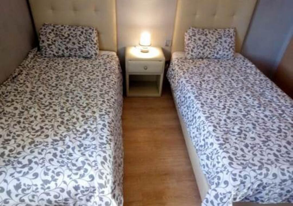 Ein Zimmer mit zwei Betten, jeweils mit einem gemusterten Überwurf, einem Nachttisch mit Lampe und Holzboden.