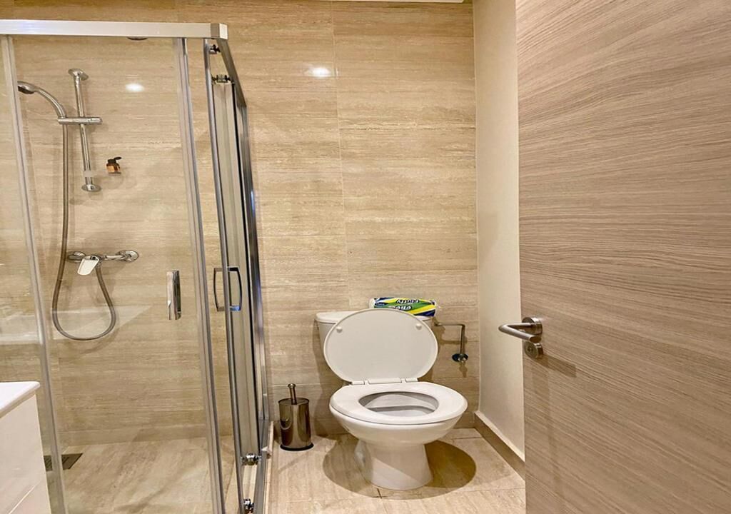 A modern bathroom with a glass-enclosed shower, a white toilet, and a wooden floor.
