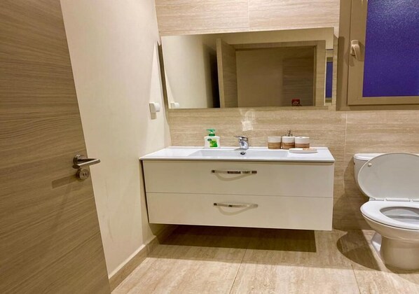 A modern bathroom with a white vanity, a mirror, a sink, and a toilet.