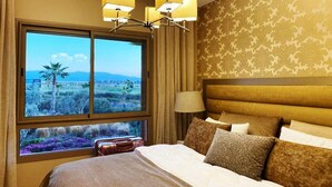 Une chambre d’hôtel avec un grand lit, un lustre, une vue sur l’extérieur et un mur orné de motifs.