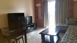 En stue med TV, sofa, sofabord og et spiseområde med stole.