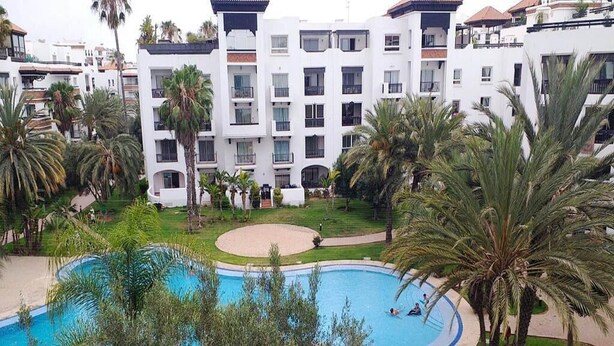 Et hotel med swimmingpool omgivet af palmer og en velholdt græsplæne.
