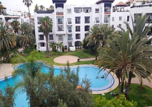 Un hotel con piscina rodeada de palmeras y un césped bien cuidado.
