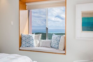 Quarto com uma janela ampla que oferece uma vista panorâmica, uma cama com cobertor branco e uma obra de arte emoldurada na parede.