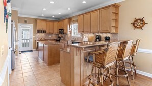 A kitchen with wooden cabinets, a large island with bar stools, a ship's wheel decoration, and a door with a window. - 5 bedrooms, 4 bathrooms,  2nd Row Home w/ Heated Pool! (Supply)