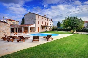 Una villa con piscina, mobiliario exterior y césped cuidado.