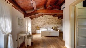 A bedroom with a stone wall, wooden ceiling beams, a bed, a bedside table, and a chair. - Villa with pool, sauna, sun terrace and WIFI (Golaš)
