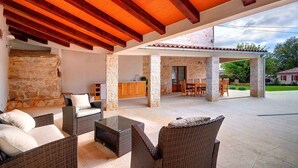 An outdoor covered patio with wicker furniture, stone pillars, and a stone wall. - Villa with pool, sauna, sun terrace and WIFI (Golaš)