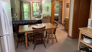 Een gezellige woonkamer met een eettafel, stoelen, een bank en een keukenhoek met een koelkast en een slowcooker.