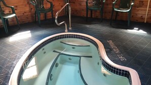 Een hottub met betegelde rand, omringd door een geribbelde vloer en houten wanden met twee ramen.