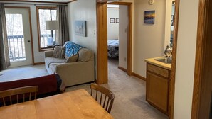 Een gezellige woonkamer met een houten eettafel, een bank en een keuken die zichtbaar is door een open deur.