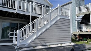 A two-story house with a white exterior, a wooden deck, and a staircase leading to the upper floor. - Waterfront 2 Bedroom - 2 Blocks from the Beach - Premium Location (Ocean City)