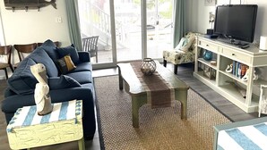 A living room with a sofa, a coffee table, a television on a stand, and a bookshelf. - Waterfront 2 Bedroom - 2 Blocks from the Beach - Premium Location (Ocean City)