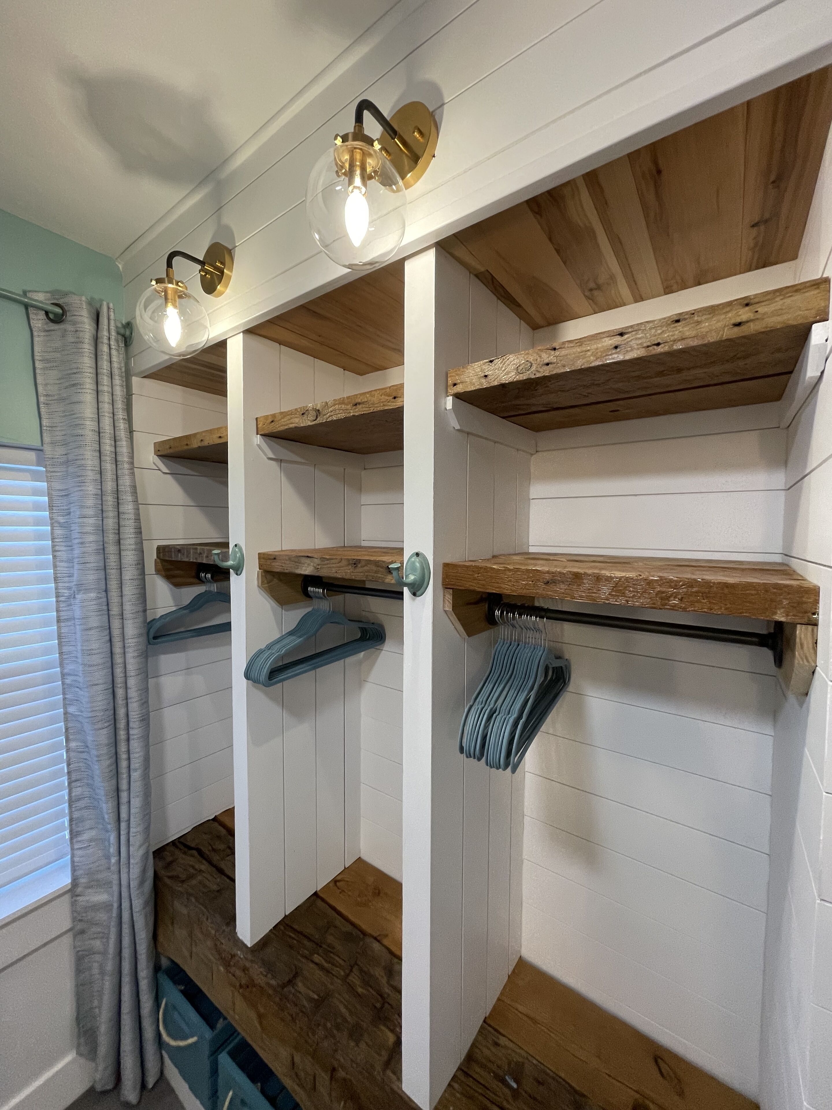 Une pièce avec des étagères en bois, un luminaire suspendu et une fenêtre avec des stores.