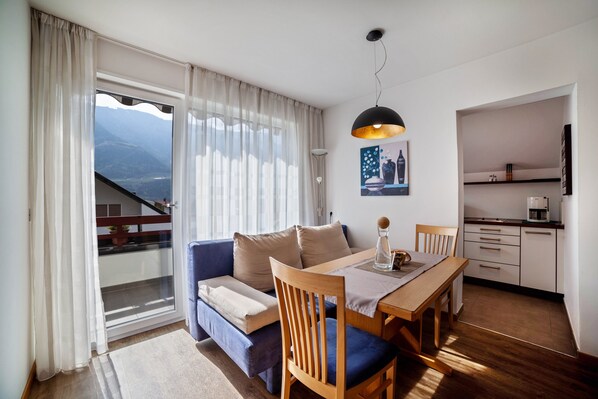 Un salon moderne comprenant un canapé, une table à manger et des chaises, un coin cuisine et une grande fenêtre avec des rideaux.