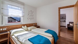 A bedroom with two beds, a window with sheer curtains, a wall decoration, and a view of a building outside. - Apartment "Schnitzer - Enzian" with Mountain View, Wi-Fi, Balcony & Garden (Rabland/Partschins)