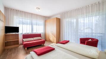 Una camera d'albergo con una TV, un divano rosso, un letto, una poltrona rossa e un armadio.