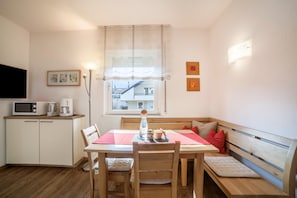 A compact living space with a kitchenette, a dining table, a bench, and a window with a view. - Apartment "Schnitzer - Hagebutte" with Mountain View, Wi-Fi, Balcony & Garden (Rabland/Partschins)