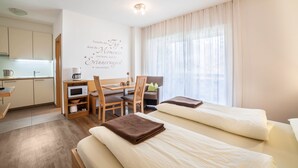 Habitación de hotel con kitchenette, zona de comedor, dos camas y un amplio ventanal con cortinas.