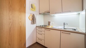 Cocina con armarios de madera, un lavamanos de acero inoxidable y una tetera.
