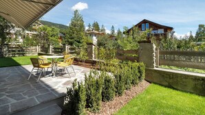 A patio with stone flooring and yellow chairs, surrounded by greenery and a wooden fence. - Premium Apartment Hofer Sandra – Fast Internet, Free Parking (Niederdorf)