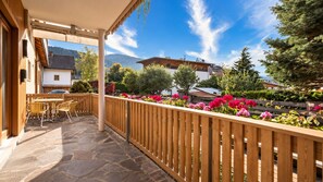 Una terrazza esterna con pavimento in pietra, arredi in legno e ringhiera in legno.