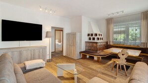 A modern living room with a flat-screen TV, a sofa, a glass coffee table, a wooden bench, and a view of a bedroom through an open door. - Premium Apartment Hofer Sandra – Fast Internet, Free Parking (Niederdorf)