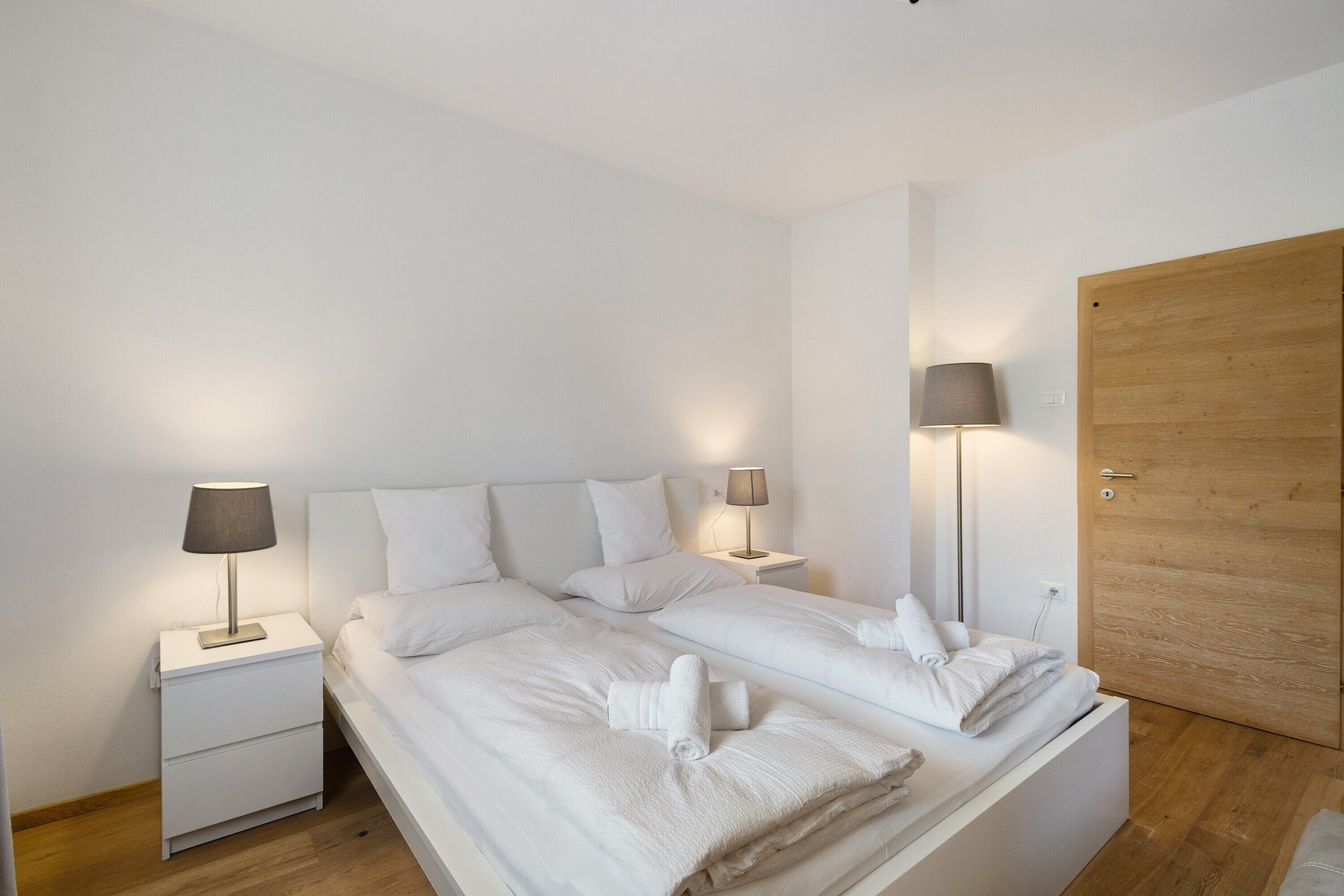 A bedroom with two beds, bedside lamps, a wooden door, and a nightstand.