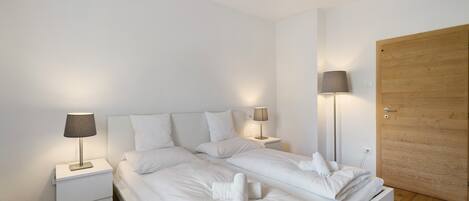 A bedroom with two beds, bedside lamps, a wooden door, and a nightstand.