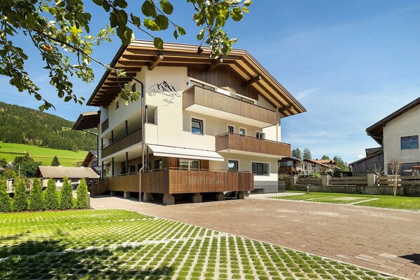 A multi-story hotel with balconies, a mountain view, and a paved courtyard. - Premium Apartment Hofer Heidi – Fast Internet, Free Parking (Niederdorf)