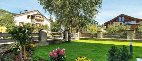 A residential area with two houses, a well-maintained lawn, and a variety of flowering plants.