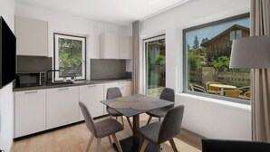 A modern kitchen with a dining area, large windows, and a view of a wooden house. - Premium Apartment Hofer Maria – Fast Internet, Free Parking (Niederdorf)