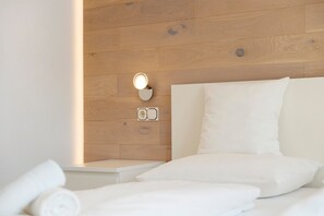 Une chambre d’hôtel avec une tête de lit en bois, une lampe de chevet et des serviettes blanches soigneusement pliées.