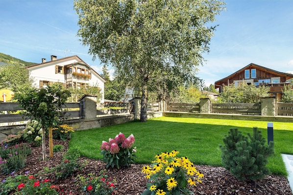A residential area with two houses, a well-maintained lawn, and a variety of flowering plants.