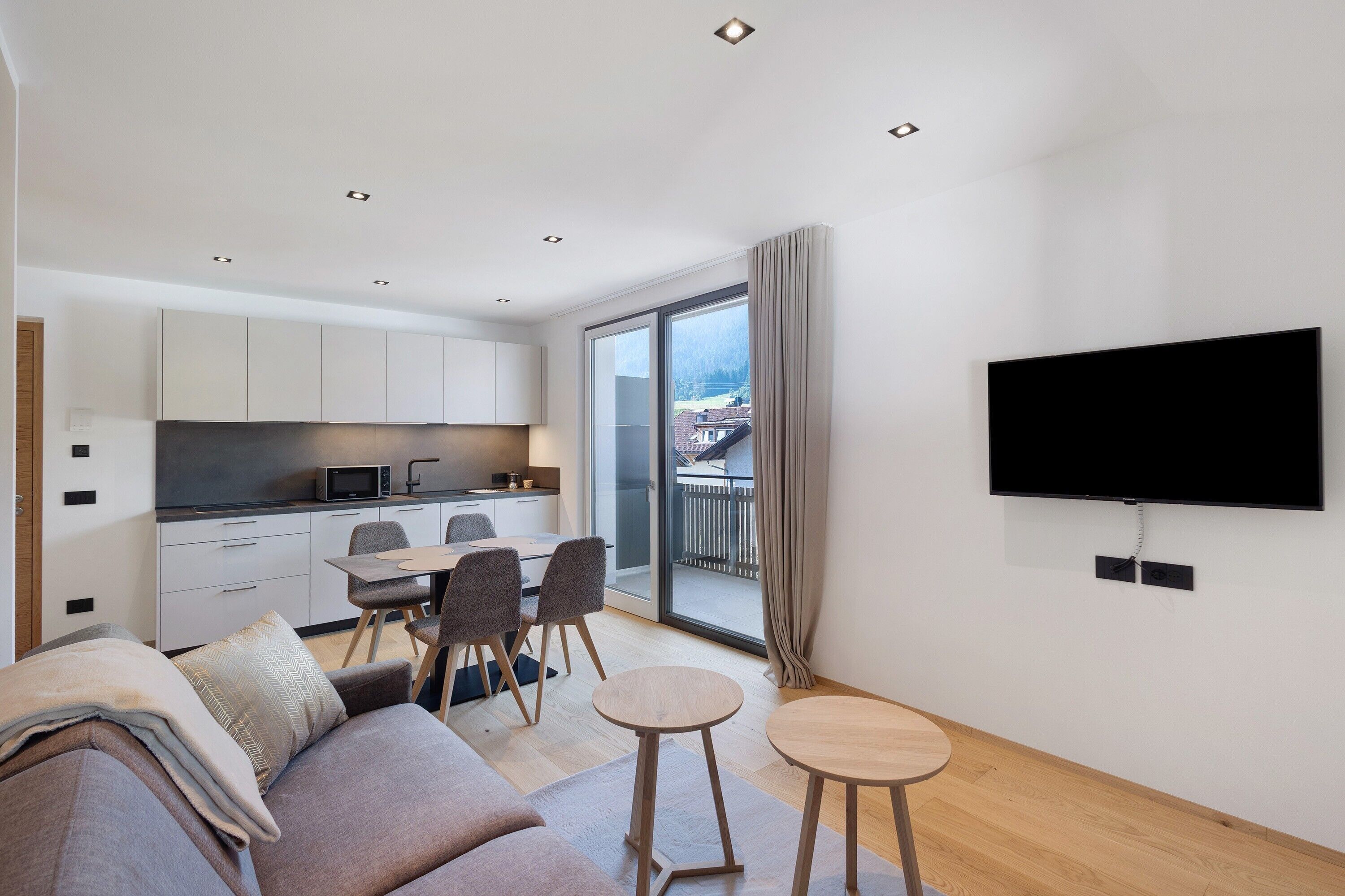 A modern apartment with a kitchen, dining area, living room, and a balcony with a TV.