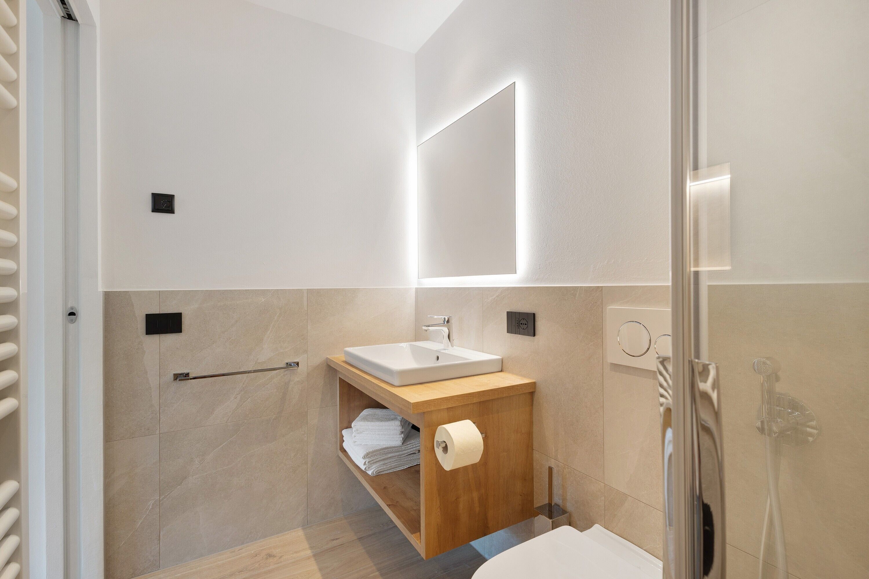 Un baño moderno con un mueble de tocador de madera, un espejo grande, ducha y retrete.