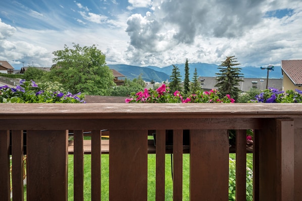 A wooden bench with a view of a garden, houses, and mountains in the background.