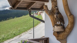Una escultura de madera de un águila sobre una rama de árbol, un banco de madera y una vista de un paisaje verde con montañas al fondo.