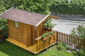 A wooden cabin with a sloped roof, a balcony with potted plants, and a wooden fence surrounding the property.