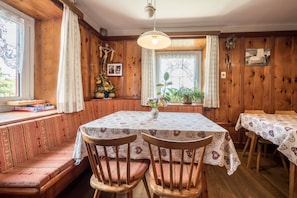 A dining area with a wooden bench seating, a table with a patterned tablecloth, and a window with curtains.