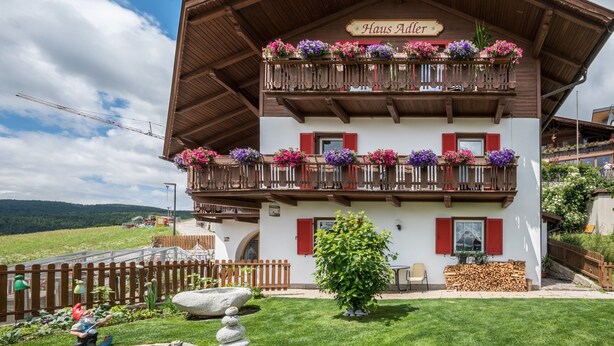 Un edificio de dos pisos con un balcón decorado con flores, un letrero que dice 'Haus Aalter' y un césped bien cuidado.