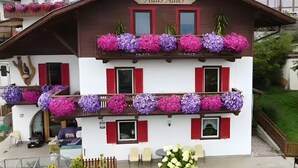 Un edificio de dos plantas con un letrero que dice 'Haus Adler', balcones con macetas de flores y un pequeño espacio de asientos al aire libre.