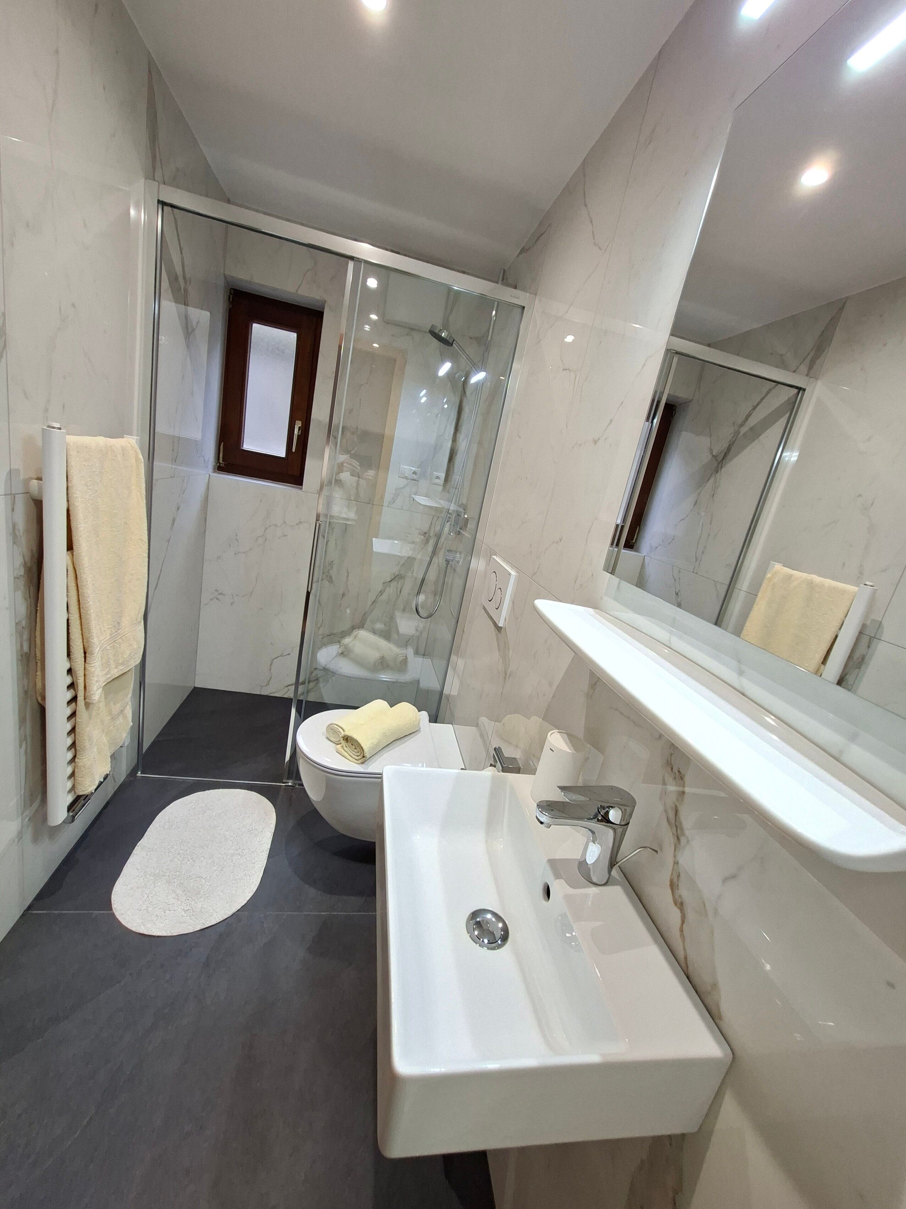 Une salle de bain moderne avec une douche en verre, un lavabo blanc et un sol carrelé en marbre.