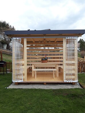 Une structure de pergola en bois, avec un banc et un jardinier au centre.