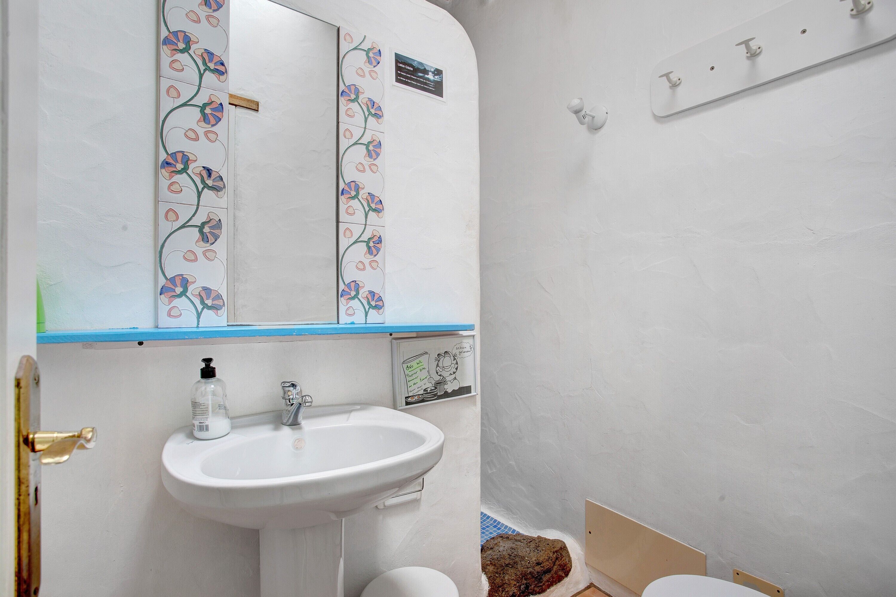 A bathroom with a white sink, a mirror with floral tiles, and a blue countertop.