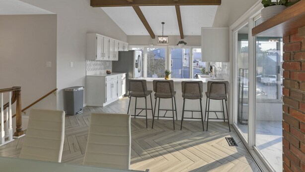Een moderne keuken met witte kasten, een centraal eiland met barstoelen, en grote ramen met uitzicht naar buiten.