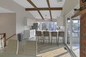 Une cuisine moderne avec des meubles blancs, un îlot central doté de tabourets de bar et de grandes fenêtres offrant une vue sur l’extérieur.
