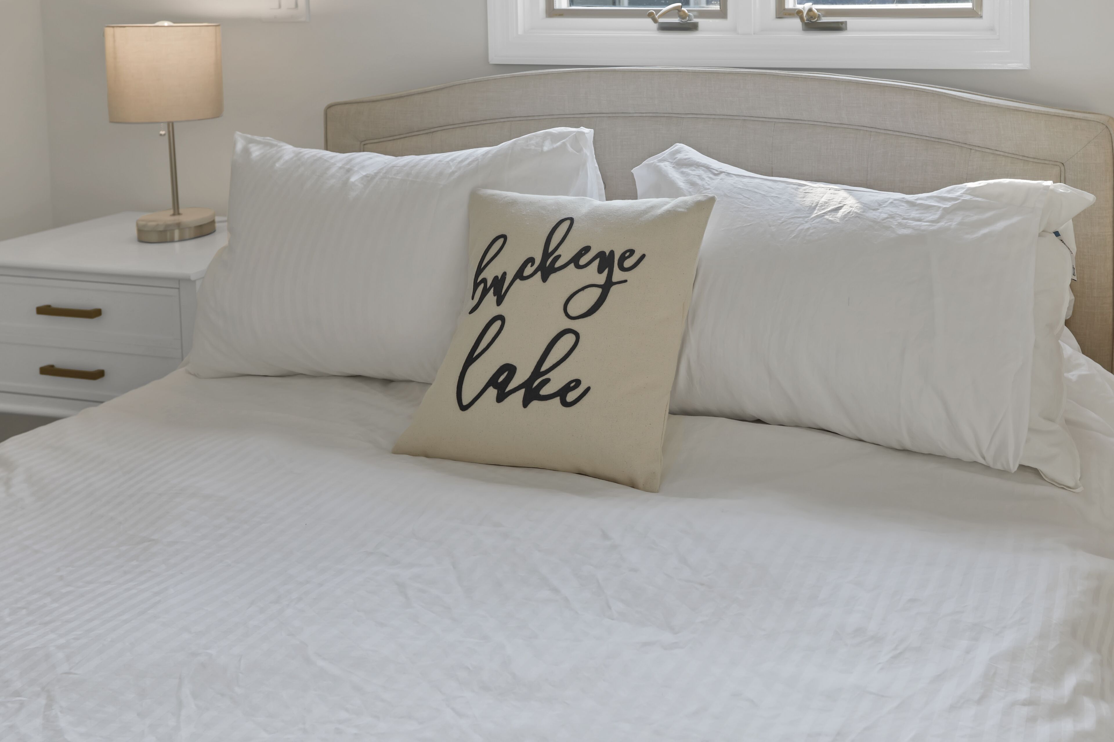 A neatly made bed with white linens and a pillow with text.